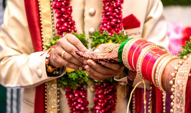 Beautiful photo of a ring ceremony being held as per Hindu rituals. Bridegroom is putting a ring to her Bride. Both dressed in traditional hindu marriage attire.